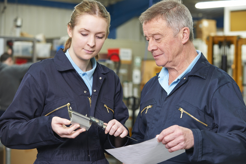 Young woman and older man examine a component in a factory